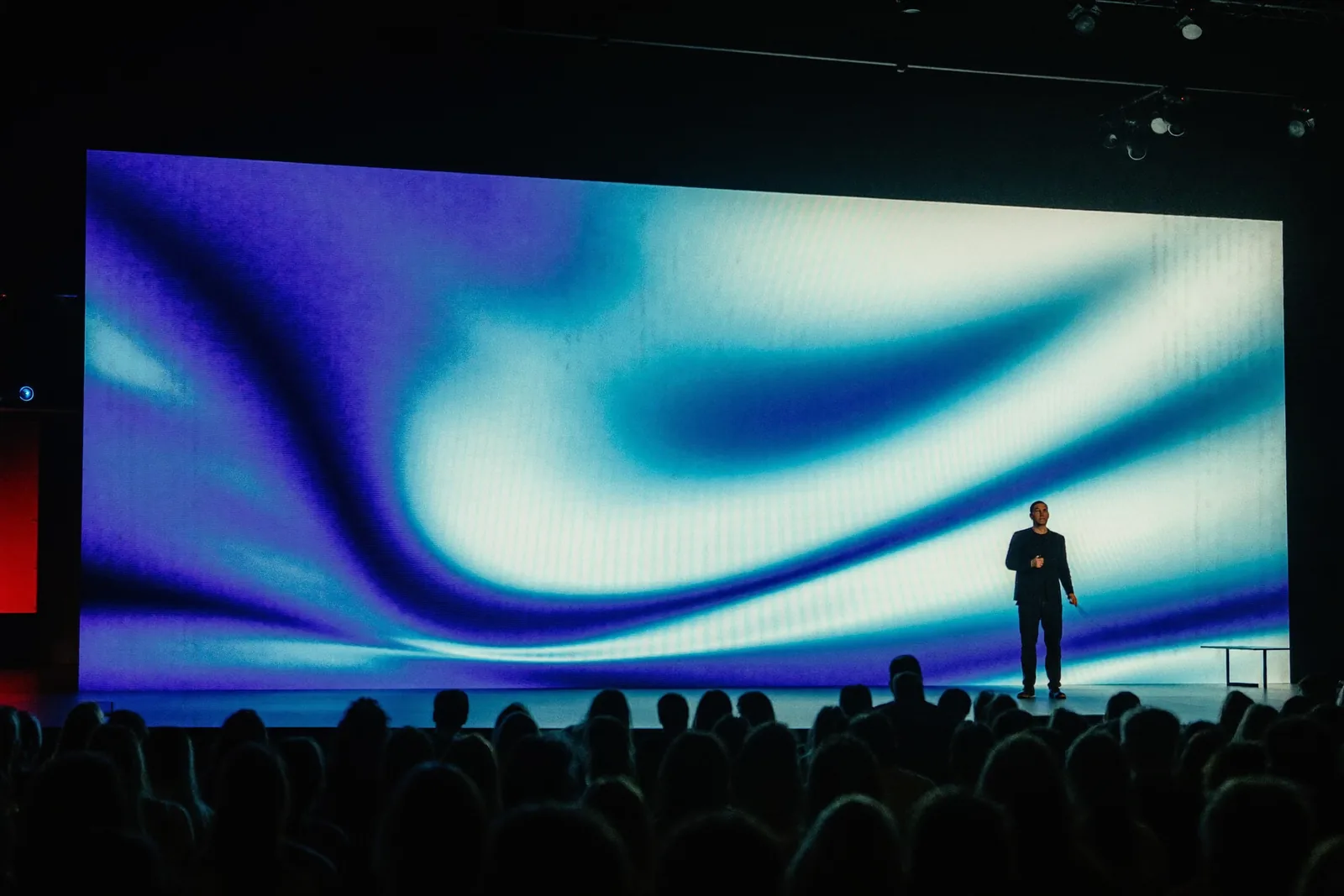 Auditorio a oscuras con una pantalla LED enorme de degradados azules y la silueta del ponente delante.